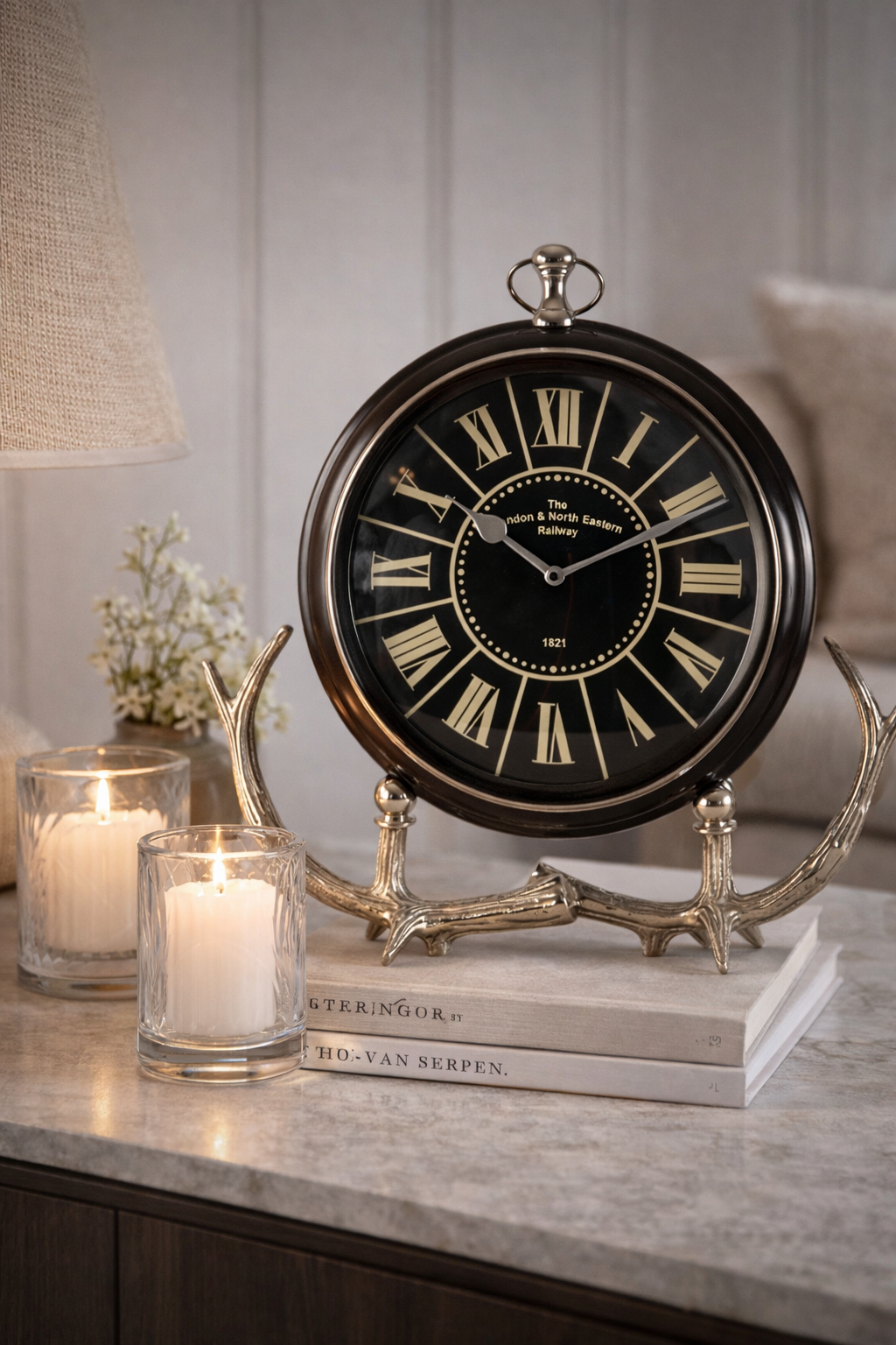Decorative clock with antlers on a table with candles and books