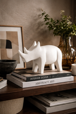 White rhinoceros sculpture on books with a vase and plant in the background