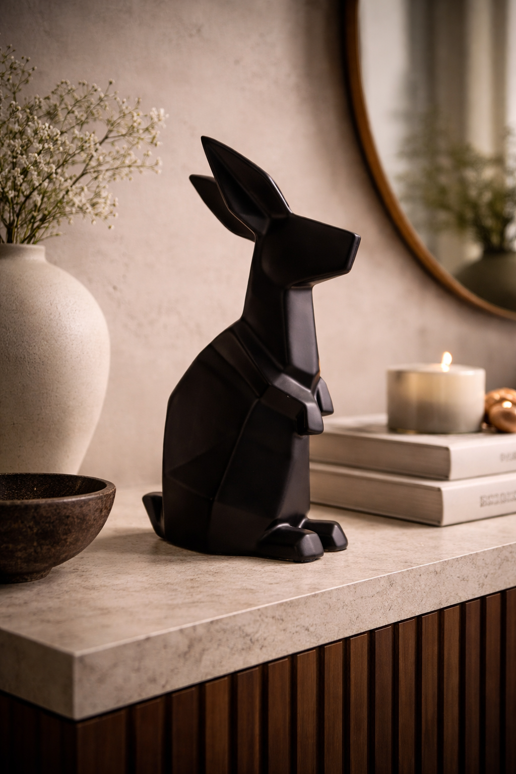Black rabbit sculpture on a surface with a vase, books, and candle in the background.