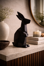 Black rabbit sculpture on a surface with a vase, books, and candle in the background.