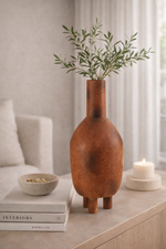 Decorative vase with greenery on a table next to books and a candle