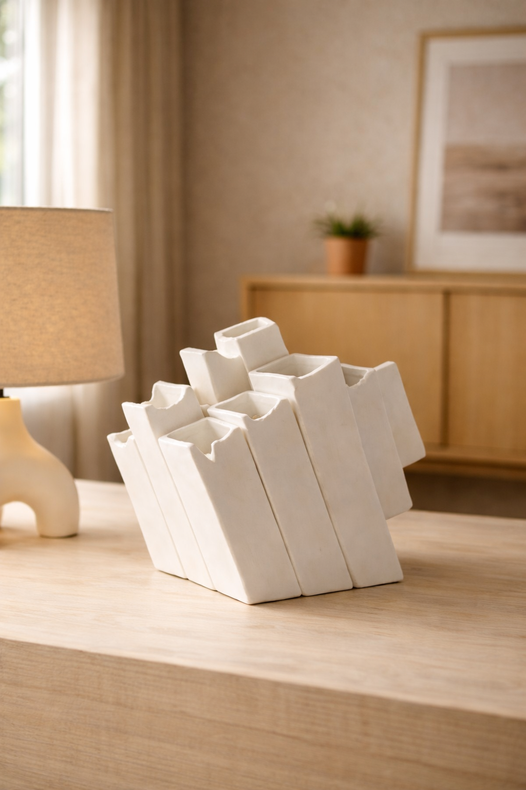 White geometric vase on a wooden surface with a lamp and framed picture in the background