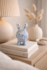 Decorative blue and white figurine on a stack of books with a lamp and vase in the background.