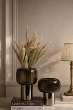 Decorative vases with a plant on a book titled 'Louis Vuitton' against a beige wall.