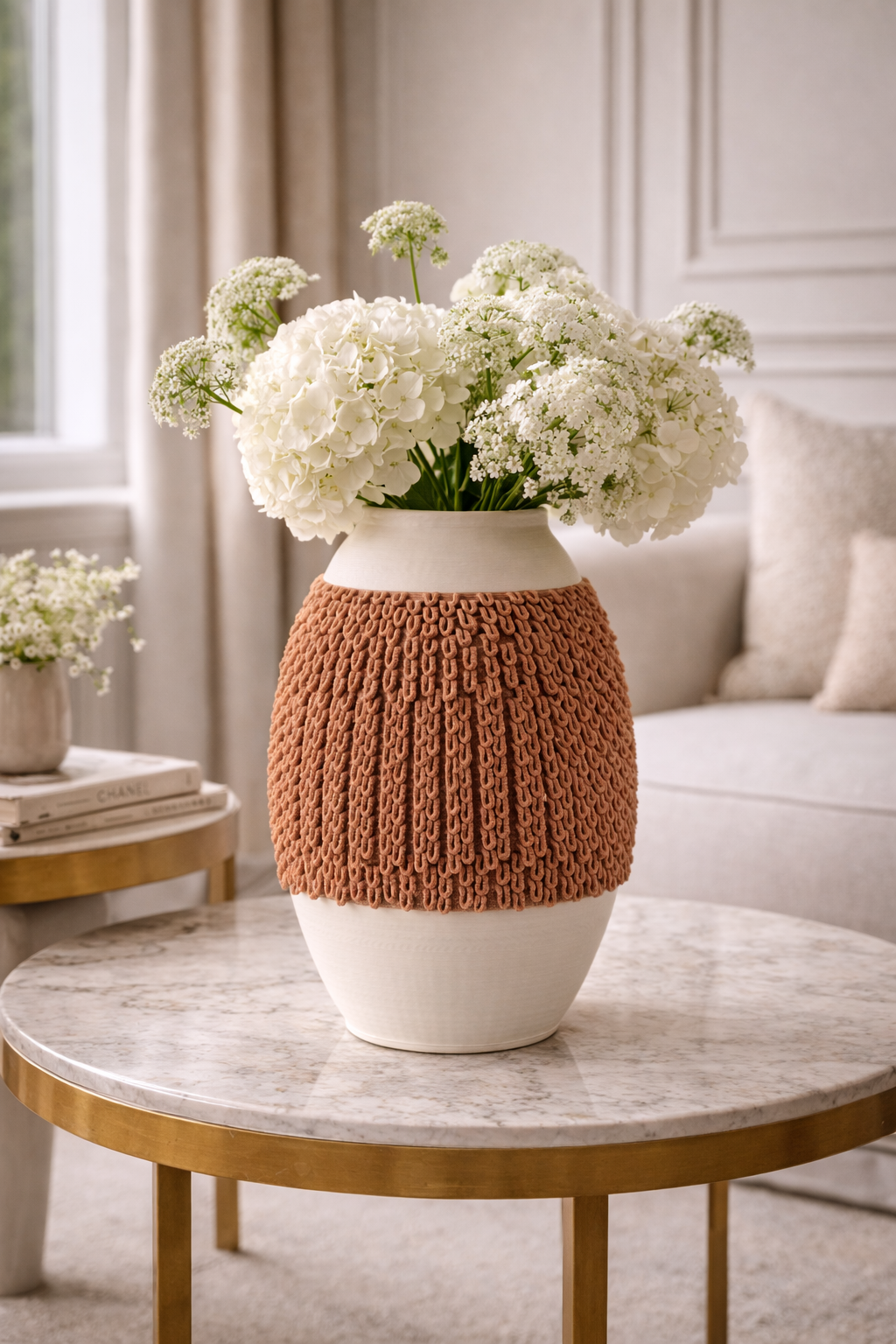 Knitted brown cover on a white vase with white flowers on a marble table in a living room.