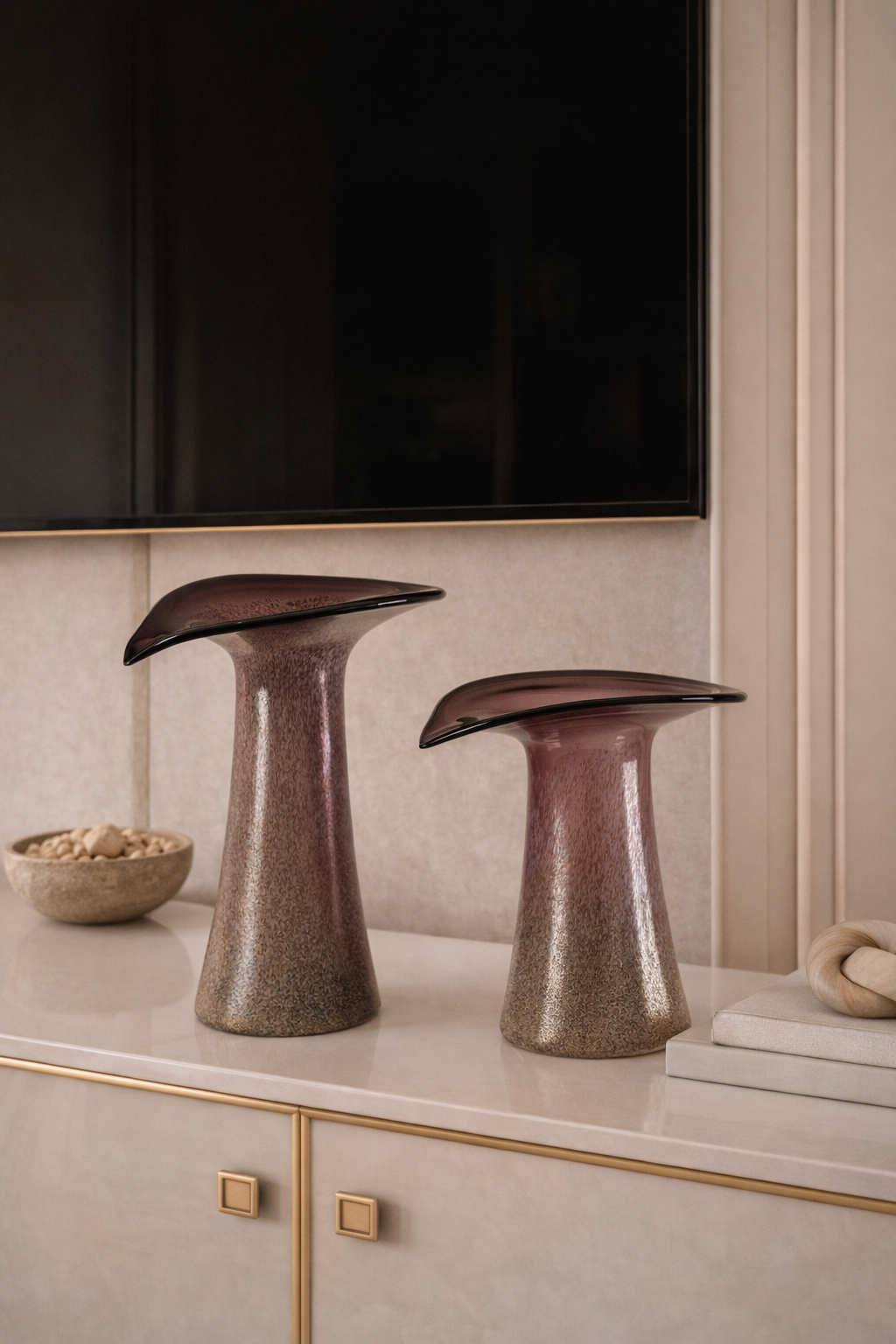 Two metallic sculptures on a shelf with a television in the background
