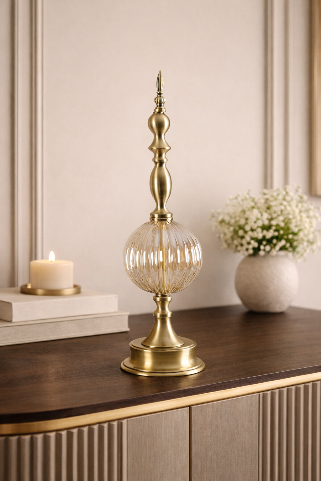 Decorative brass lamp on a wooden surface with a candle and flowers in the background.