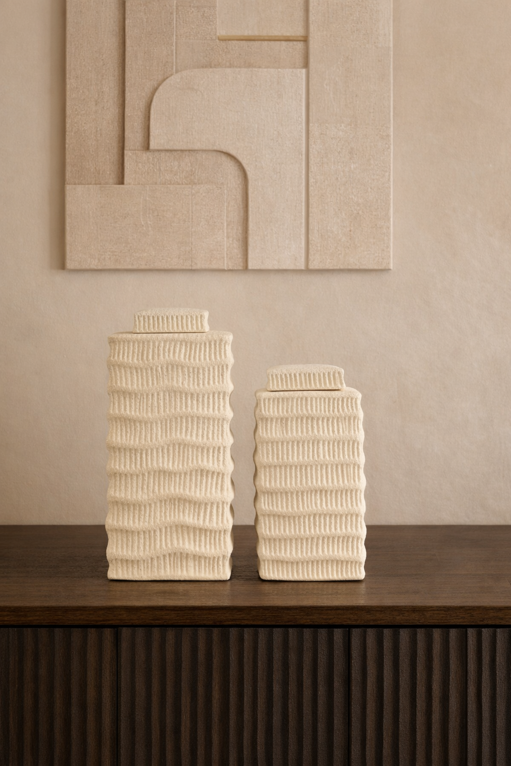 Two textured ceramic vases on a wooden surface with a neutral wall in the background
