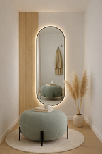 Modern interior with a large oval mirror, light green ottoman, and decorative plant.