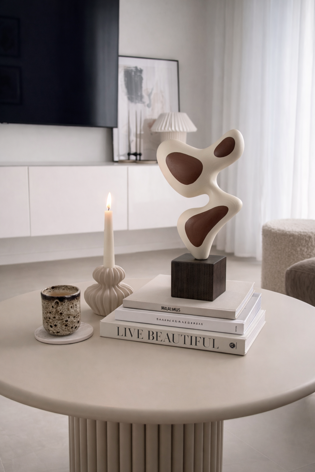 Decorative table with a candle, books, and a sculpture in a modern living room.