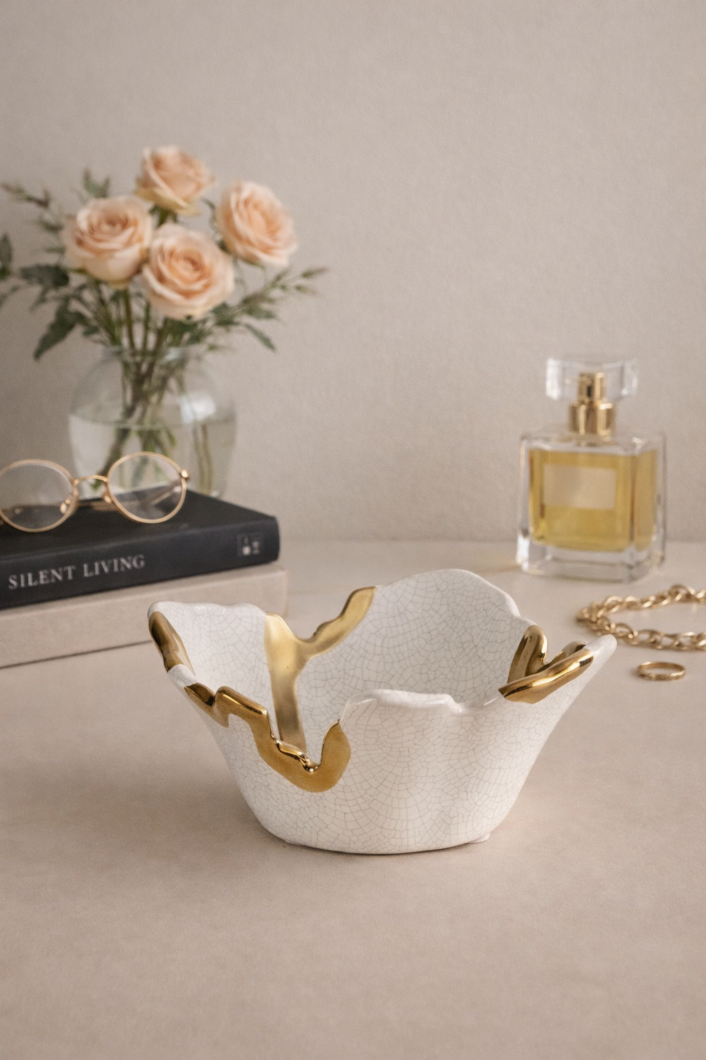 Decorative white dish with gold accents on a table with flowers and books in the background
