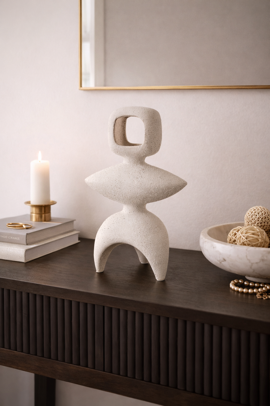 Abstract stone sculpture on a dark wooden surface with a candle and books in the background.