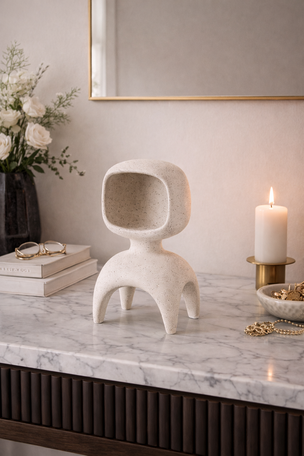 Decorative white sculpture on a marble surface with books, flowers, and a candle in the background.