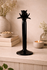 Black candle holder on a wooden surface with a candle and decorative items in the background.