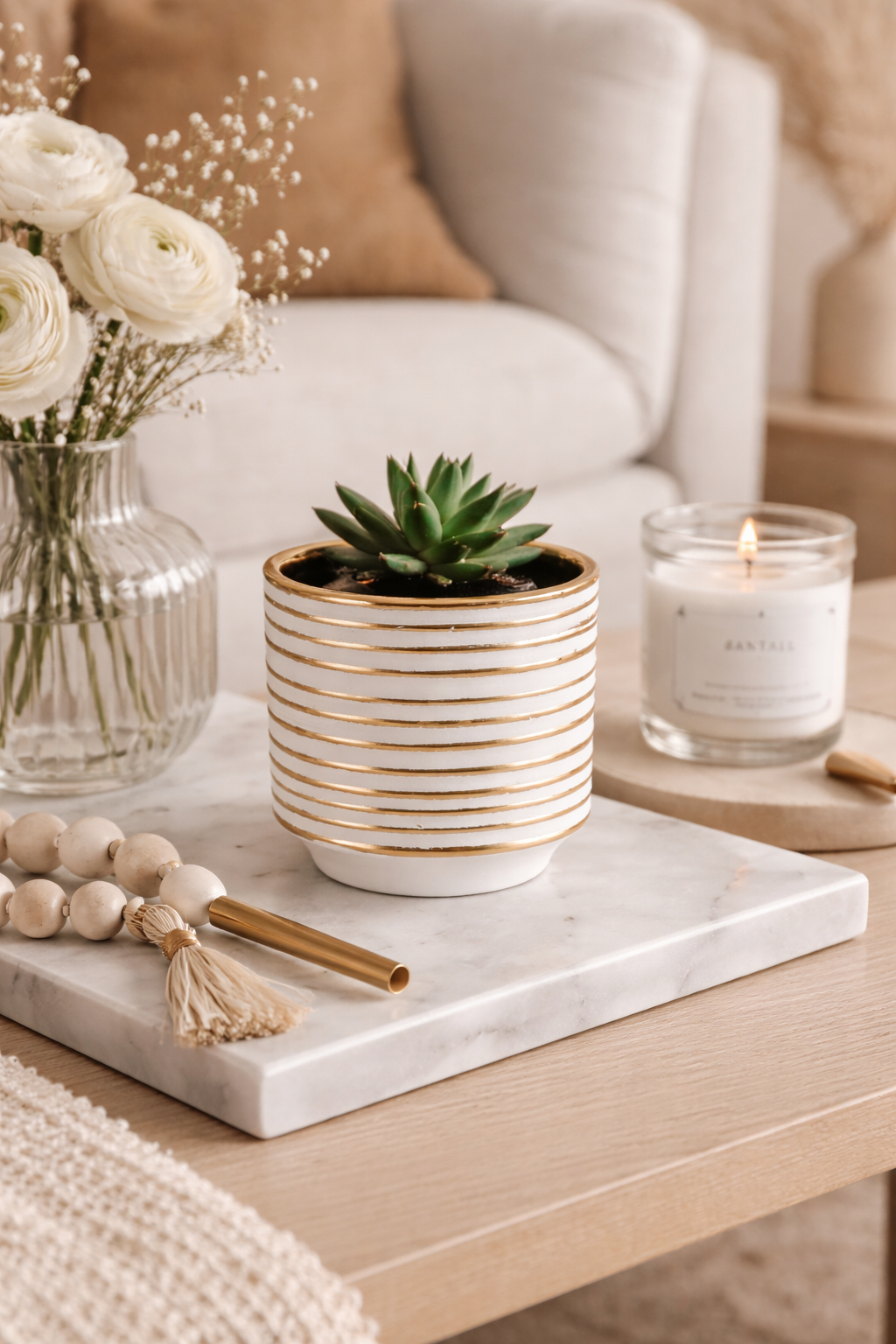 Decorative setting with a potted plant, candle, and flowers on a marble tray.