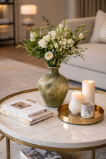 Decorative setup on a marble coffee table with flowers, candles, and books in a living room.