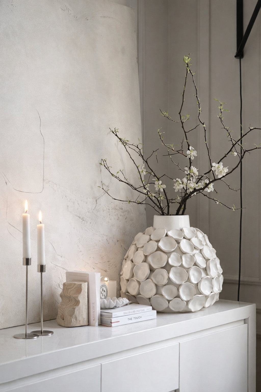 White vase with decorative shell pattern on a white surface with candles and books.