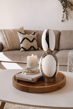 Decorative table setting with a candle, book, and sculpture on a wooden tray in a living room.