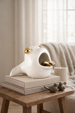 Decorative white and gold bird sculpture on books with a candle and small birds on a wooden table.
