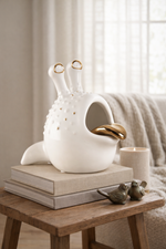 White ceramic birdhouse with gold accents on a wooden table