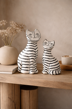 Two ceramic cat figurines on a wooden surface with a neutral background