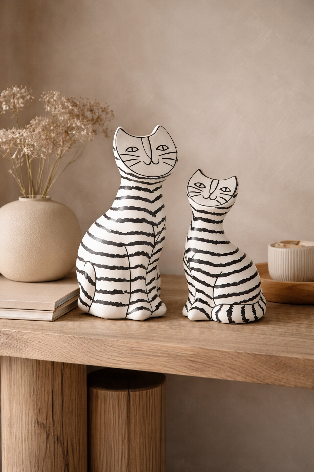 Two ceramic cat figurines on a wooden surface with a neutral background