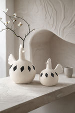 Two white ceramic birds with black spots on a light wooden surface.