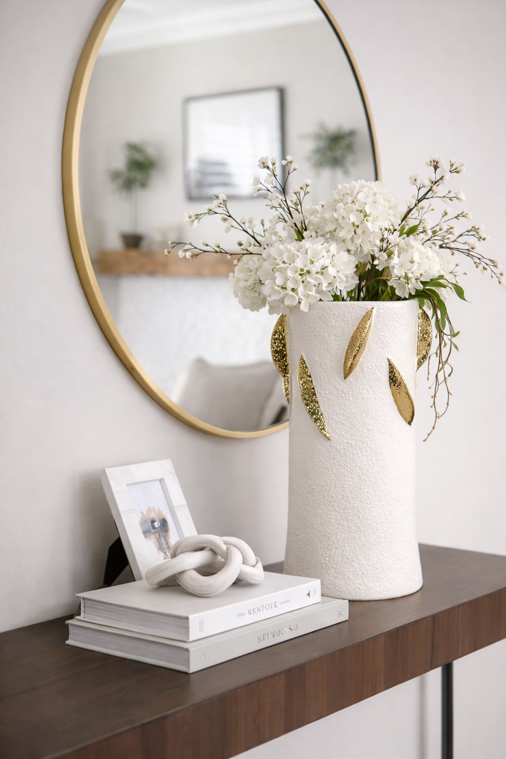 Decorative setup with a vase of white flowers, books, and a knot sculpture on a wooden surface.