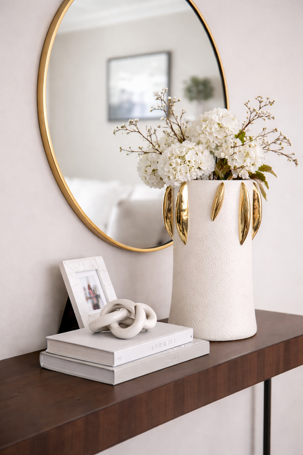 Decorative setup with a vase of white flowers, books, and a mirror on a wooden surface.