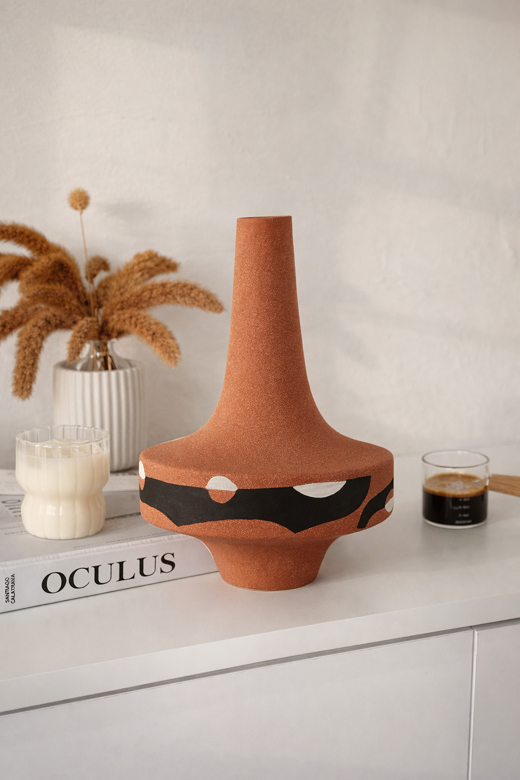 Ceramic vase with abstract design on a white surface with books and decor items.