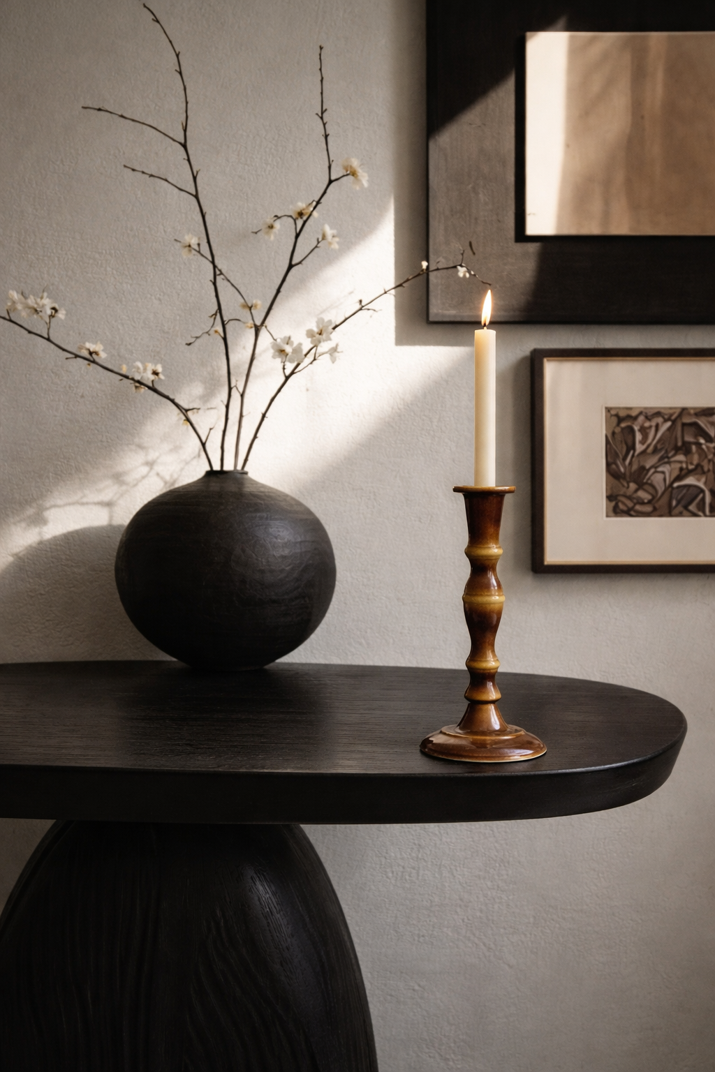 Decorative setup with a black vase, candlestick, and framed picture on a wall.