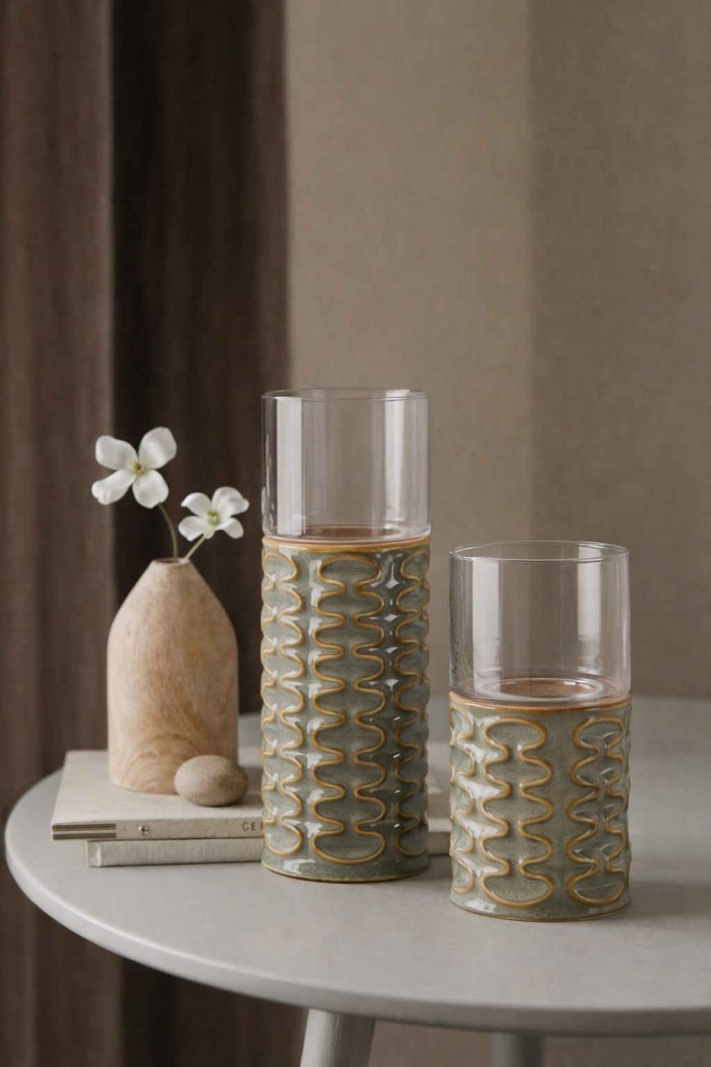 Two decorative glasses with a textured pattern on a table with a vase and flowers.