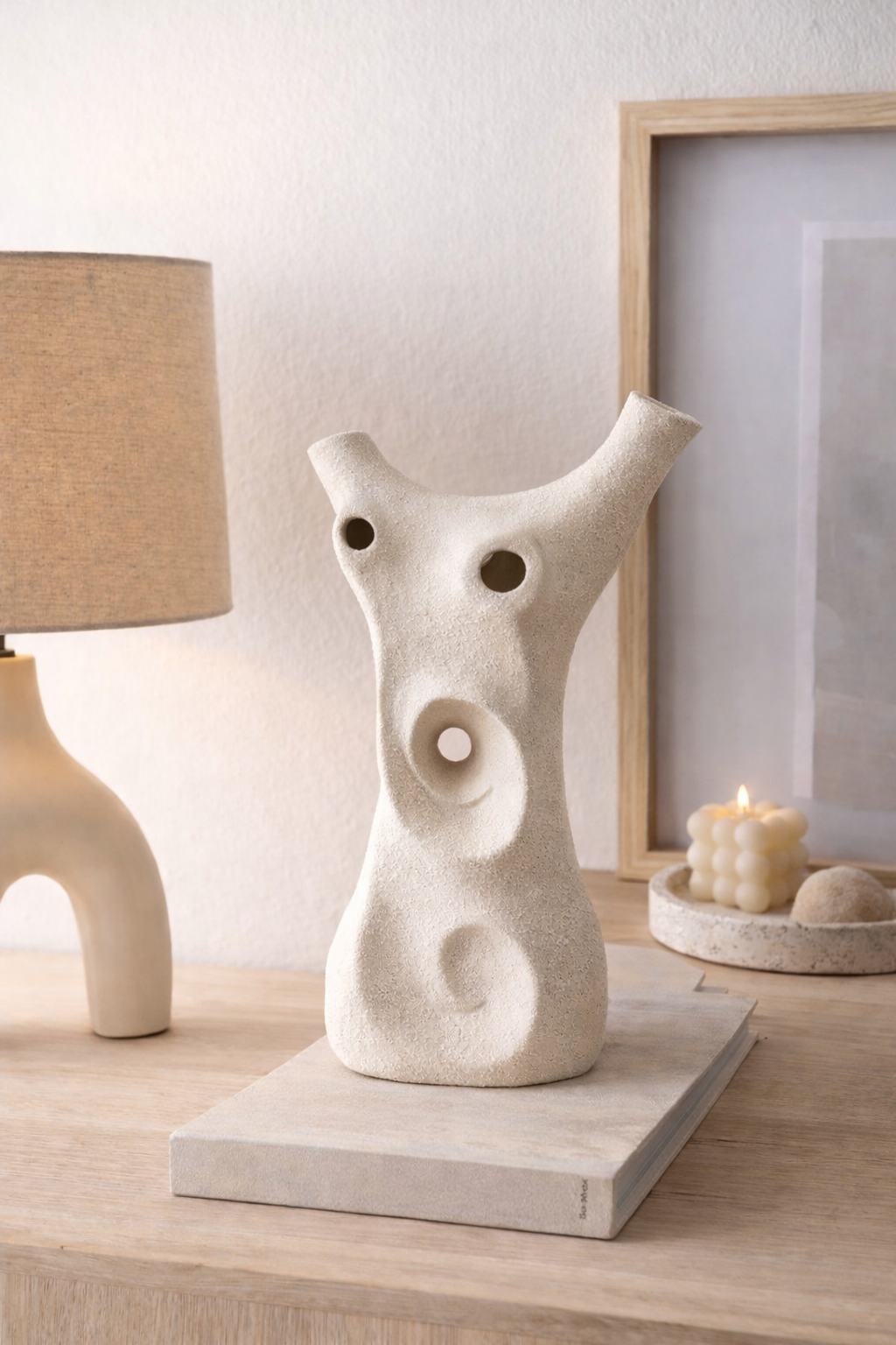 Decorative ceramic sculpture on a wooden surface with a lamp and framed picture in the background.