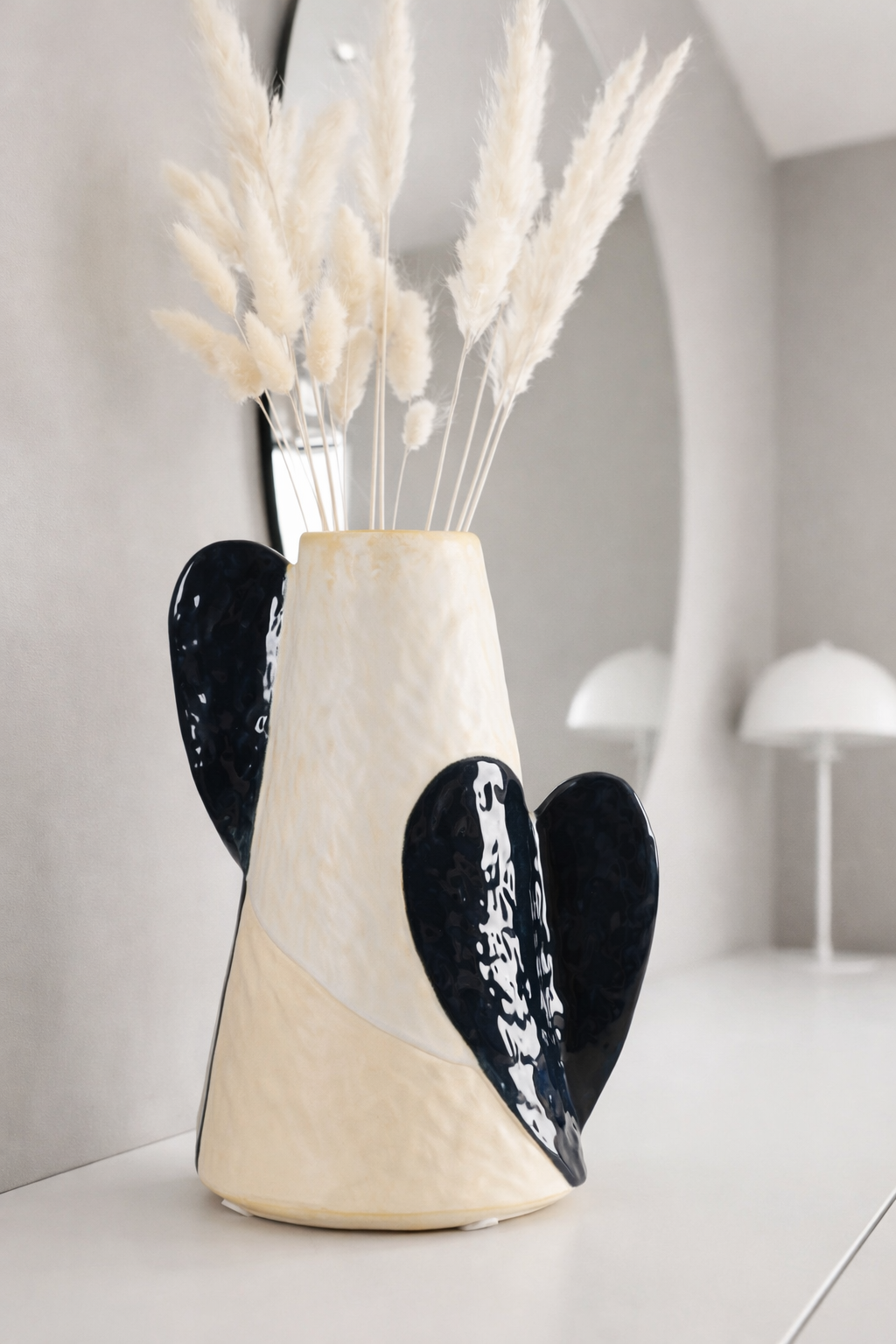 Ceramic vase with black heart designs and dried plants on a white surface.