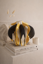 Decorative vase with black, yellow, and white design on a stack of books.