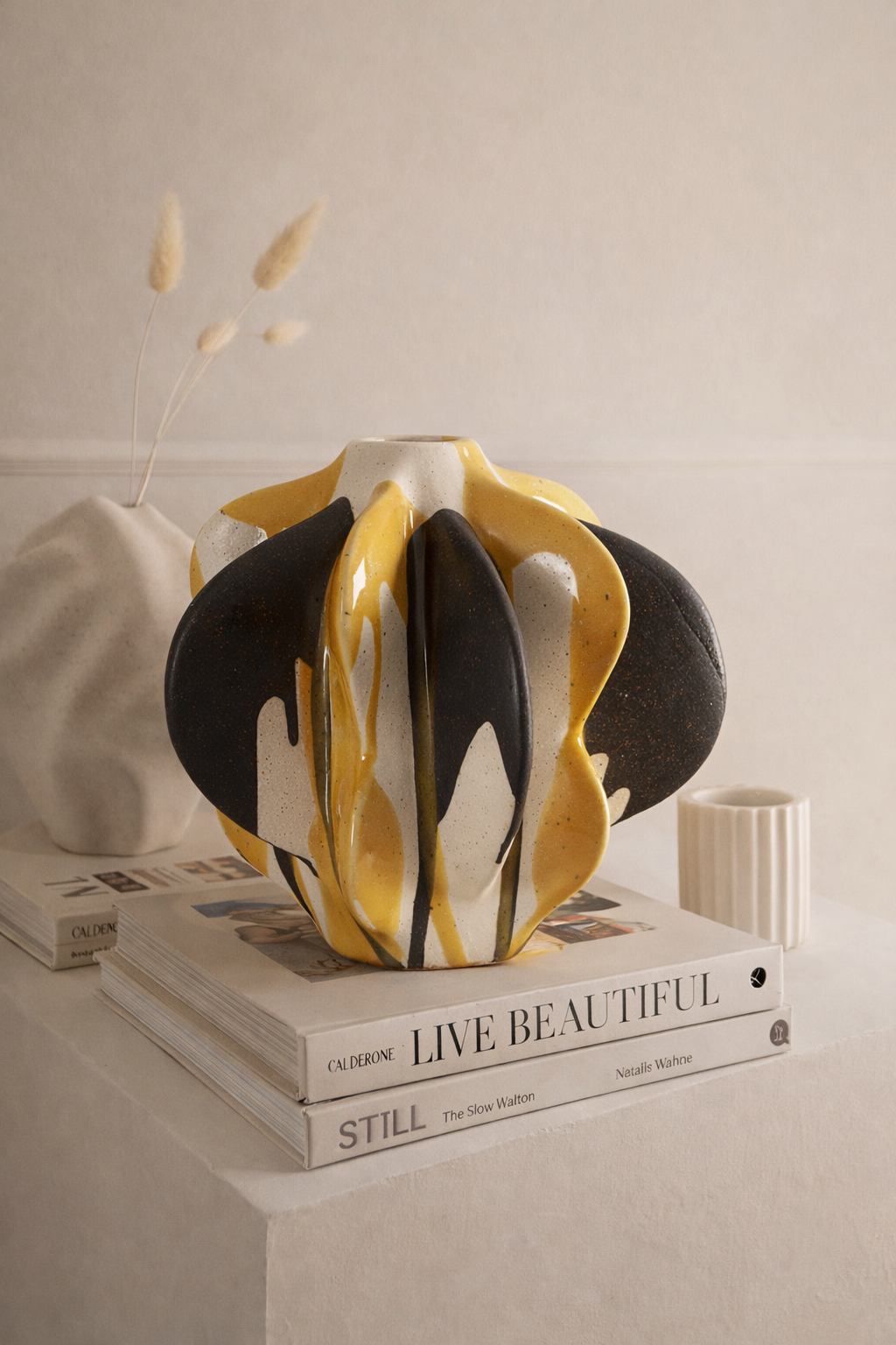 Decorative vase with black, yellow, and white design on a stack of books.
