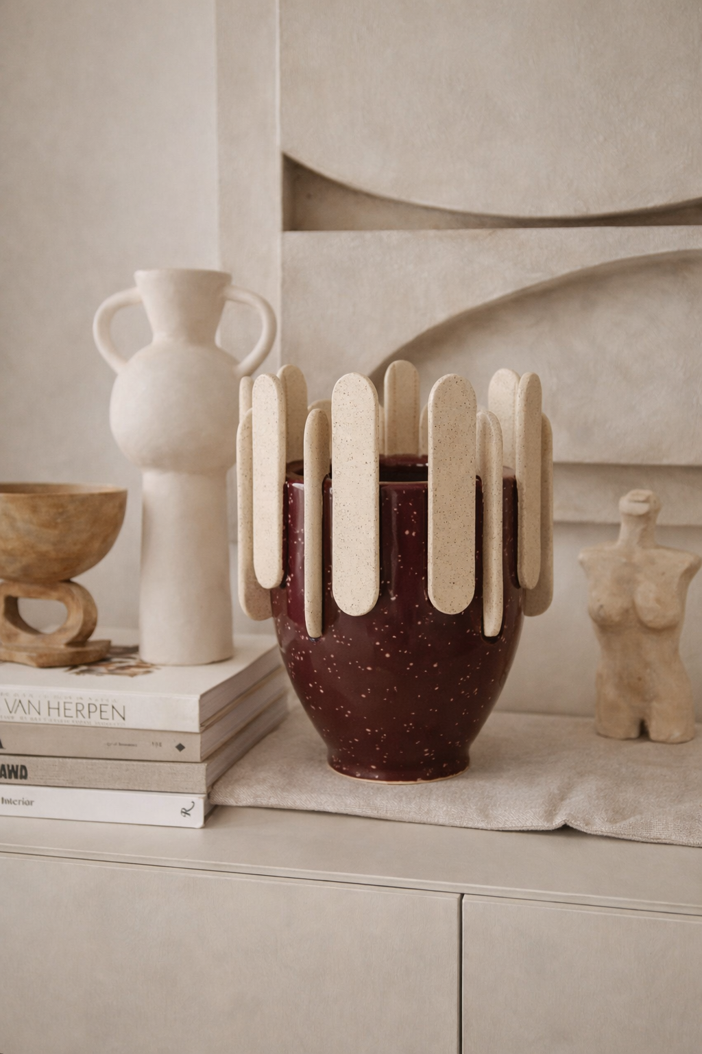 Ceramic vase with unique design on a shelf with books and other decorative items.