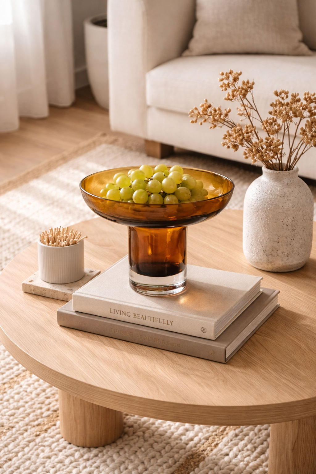Wooden coffee table with a bowl of grapes, books, and a vase in a living room setting.