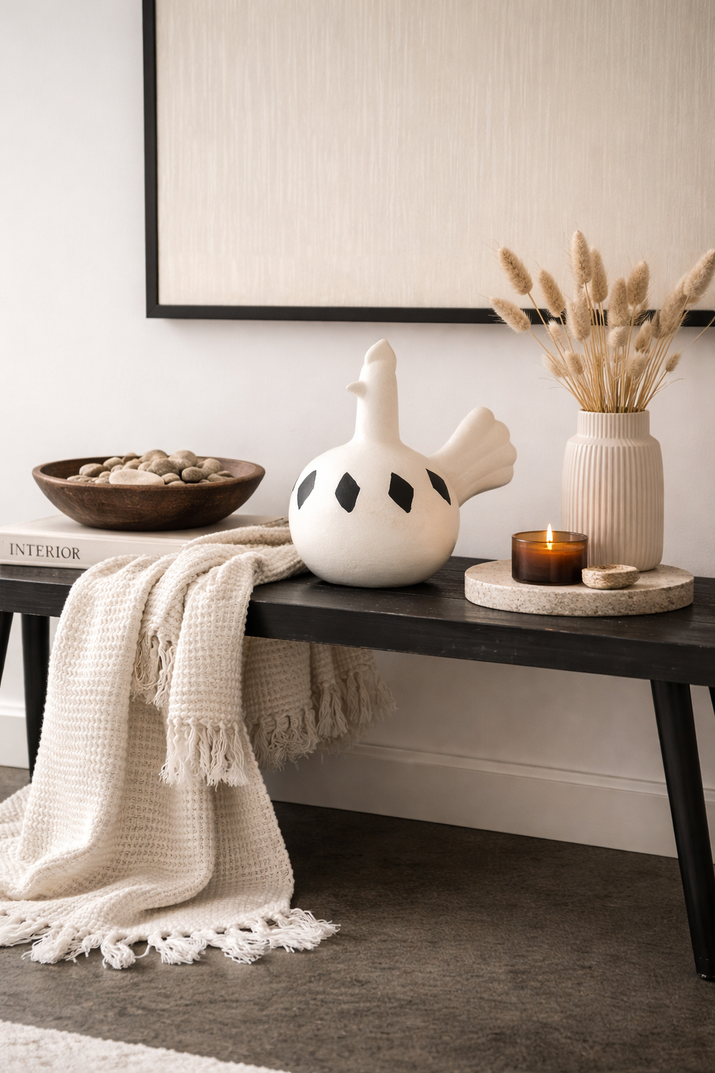 Decorative items on a console table including a ceramic goose, candle, and vase with dried plants.