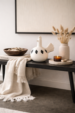 Decorative items on a console table including a ceramic goose, candle, and vase with dried plants.