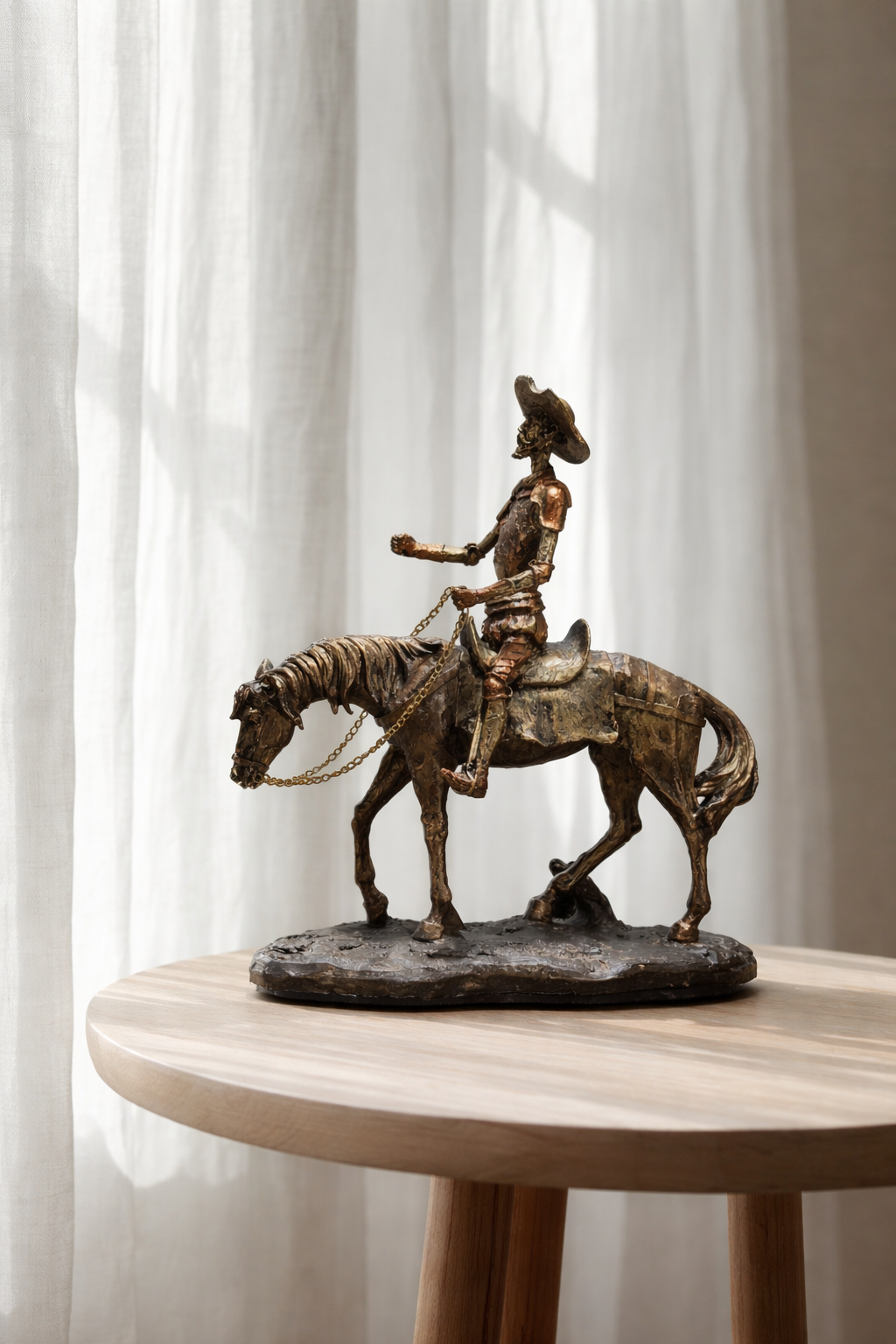 Bronze sculpture of a person on horseback on a wooden table with white curtains in the background