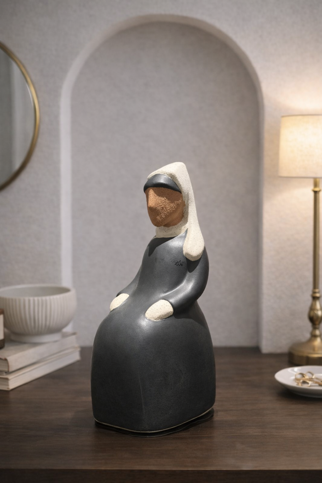 Decorative ceramic figure of a seated woman in a dark dress with white accents on a wooden surface.