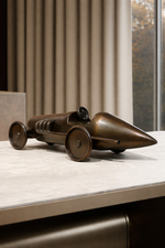 Bronze model of a vintage car on a marble surface with a neutral background