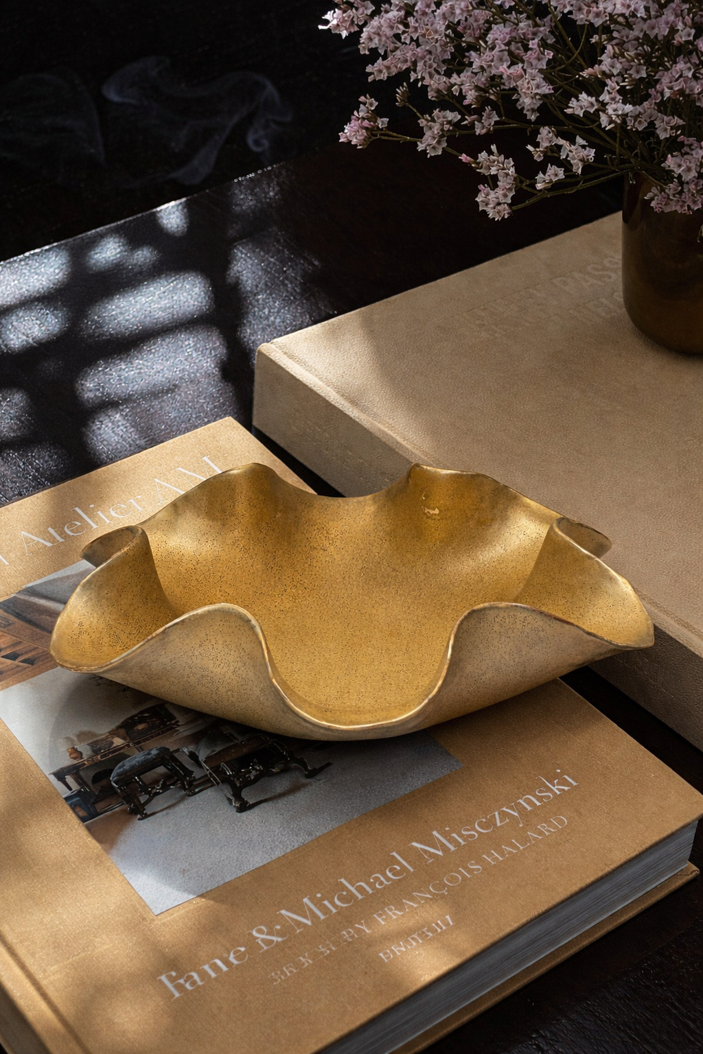 Gold leaf-shaped bowl on a book with a vase of flowers in the background