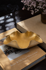 Gold leaf-shaped bowl on a book with a vase of flowers in the background