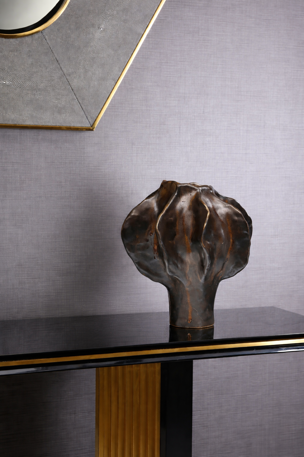 Bronze sculpture on a black and gold console table against a gray wall.