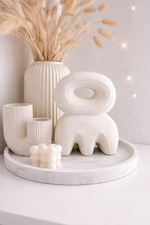 Decorative arrangement with white ceramic vases and a sculpture on a marble tray against a light gray background.