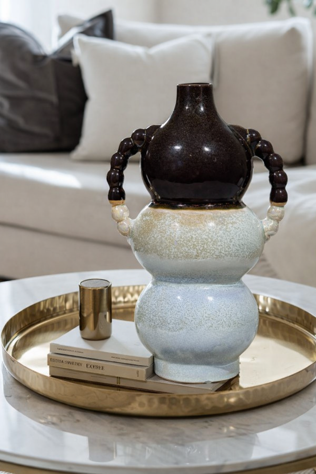 Decorative vase on a marble table with a gold tray and books in a living room setting.