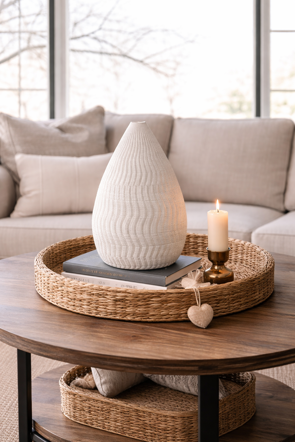 Decorative setup on a wooden coffee table with a vase, candle, and books in a living room.