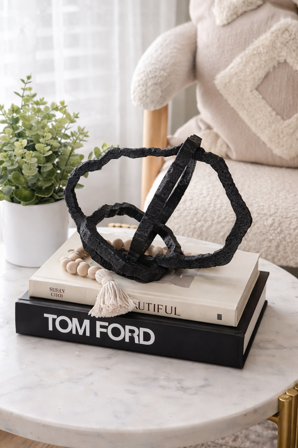 Decorative black sculpture on books with a plant and soft chair in the background